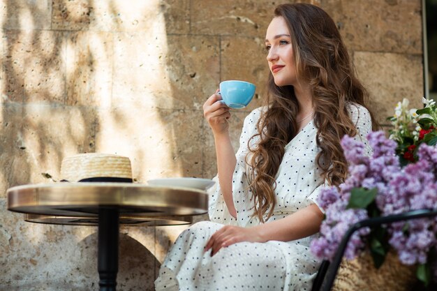 Bella donna che gode del caffè del mattino vicino al fiore lilla. Modello carino e fiori. Aromaterapia e concetto di primavera. La ragazza beve il caffè alla caffetteria.