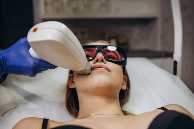 Bella donna che ha la depilazione laser e l'epilazione laser all'area delle labbra sul viso al salone di cosmetologia