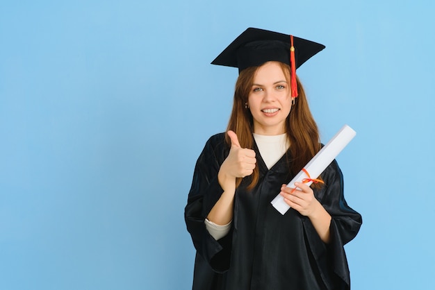 Bella donna che indossa il cappello di laurea e abito da cerimonia in possesso di laurea in piedi positivo e felice e sorridente con un sorriso fiducioso.