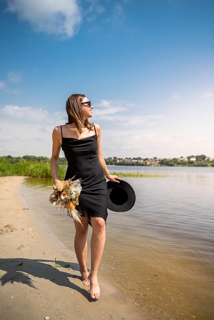 Bella donna che indossa un abito nero da cocktail in piedi sulla libertà del giorno caldo d'estate del lago d'acqua