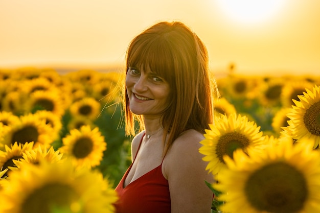 Bella donna che indossa un vestito rosso che sorride e che guarda l'obbiettivo in un campo di girasoli.