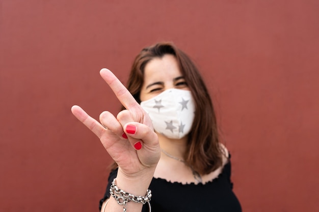 Bella donna che indossa una maschera, si diverte e fa un gesto rock and roll con la mano