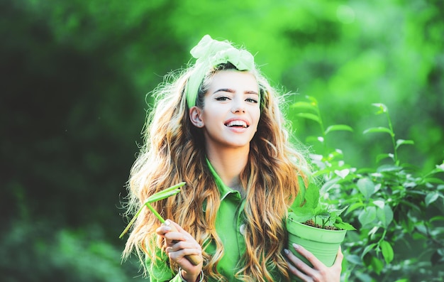 Bella donna che lavora e gioca nel bellissimo giardino Concetto di moda donna primavera Ritratto di sorridente ragazza affascinante tenere vaso di fiori e guardando la fotocamera