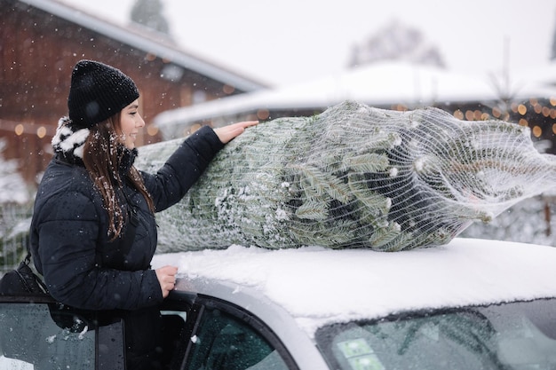 Bella donna che lega per mettere un albero di natale sul tetto dell'auto per portarlo a casa abete vivo