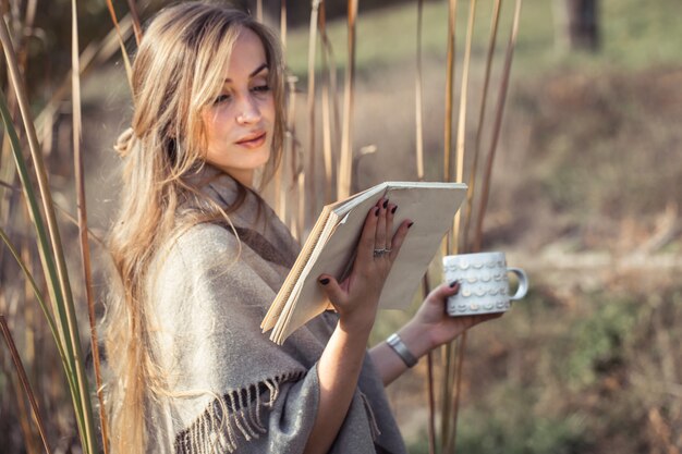 bella donna che legge un libro nella foresta di autunno