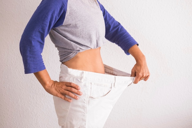 Bella donna che mostra il suo vecchio grande pantalon dopo aver perso peso a casa - fitness a casa e lavorando per stare meglio con te stesso - mangiare bene