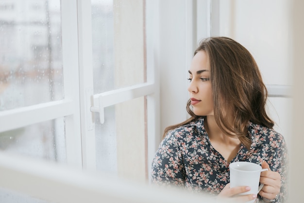 Bella donna che osserva attraverso la finestra il giorno di pioggia.