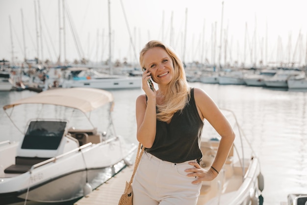 Bella donna che parla al telefono sullo sfondo del mare blu e degli yacht