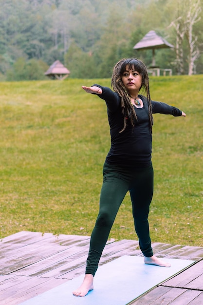 Bella donna che pratica yoga in una foresta, è latina e ha i dreadlocks.