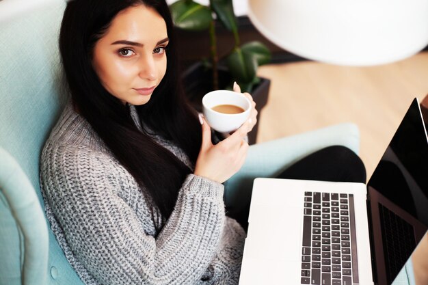 Bella donna che resta a casa e lavora al computer portatile online.