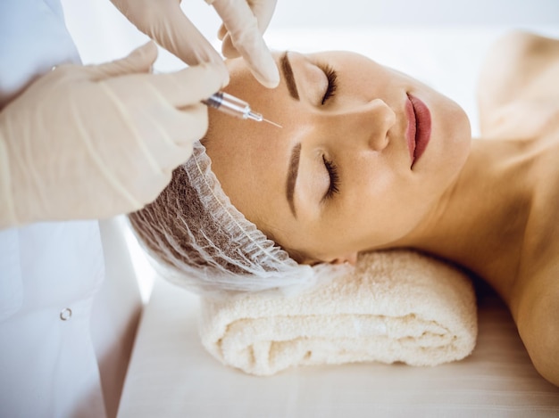 Bella donna che riceve iniezioni di bellezza con gli occhi chiusi in un centro medico medico di bellezza che fa una procedura di bellezza al viso femminile con una siringa concetto di medicina cosmetica e chirurgia