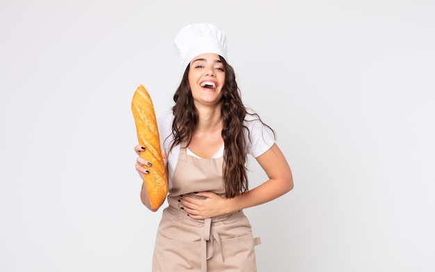 Bella donna che ride ad alta voce per qualche scherzo esilarante che indossa un grembiule e tiene in mano una baguette di pane