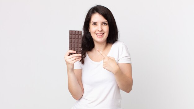 Bella donna che sembra eccitata e sorpresa indicando il lato e tenendo in mano una barretta di cioccolato