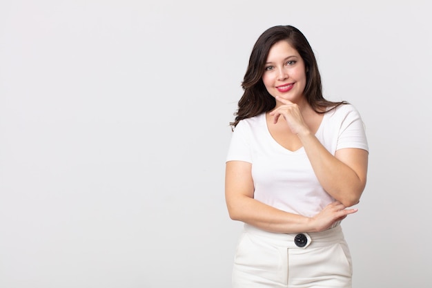 Bella donna che sembra felice e sorridente con la mano sul mento, chiedendosi o facendo una domanda, confrontando le opzioni