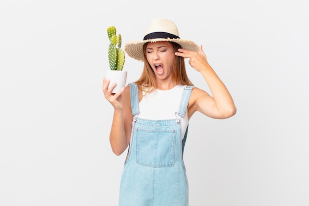 bella donna che sembra infelice e stressata, gesto suicida che fa il segno della pistola e tiene in mano una pianta decorativa di cactus