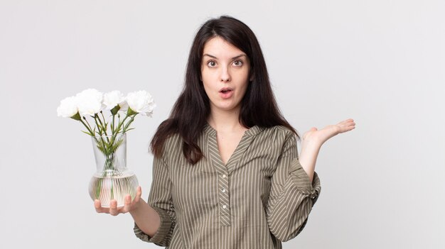 Bella donna che sembra sorpresa e scioccata, con la mascella caduta in possesso di un oggetto e con in mano un fiore decorativo. assistente agente con un auricolare