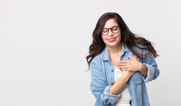 Bella donna che sembra triste, ferita e con il cuore spezzato, tenendo entrambe le mani vicino al cuore, piangendo e sentendosi depressa