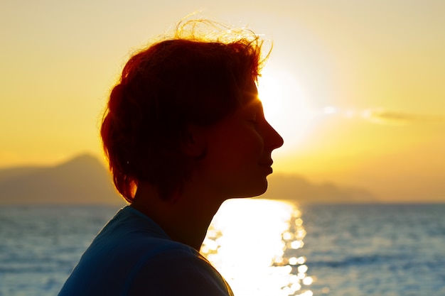 Bella donna che si distende sopra il tramonto sulla costa del mare