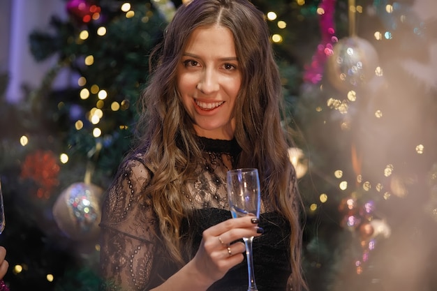 Bella donna che si diverte con un bicchiere di champagne vicino a un albero di Natale. Una donna ride, sorride, posa. Filtro antirumore e grana speciale vintage, luci sfocate.