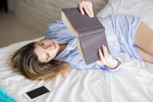 Bella donna che si rilassa a casa e sul suo letto mentre legge un libro