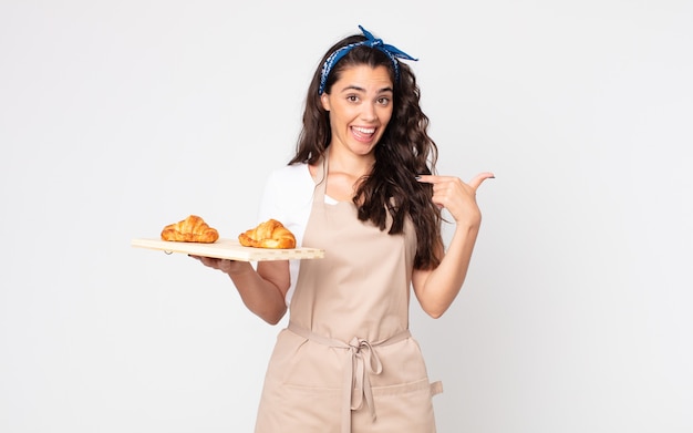 Bella donna che si sente felice e indica se stessa con un eccitato e tiene in mano un vassoio di croissant