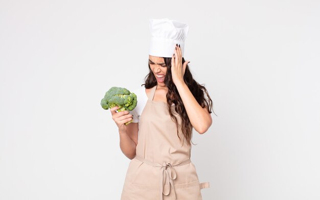 Bella donna che si sente felice, eccitata e sorpresa indossando un grembiule e tenendo in mano un broccolo