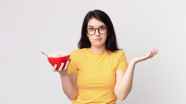 Bella donna che si sente perplessa e confusa e dubita e tiene in mano una ciotola per la colazione