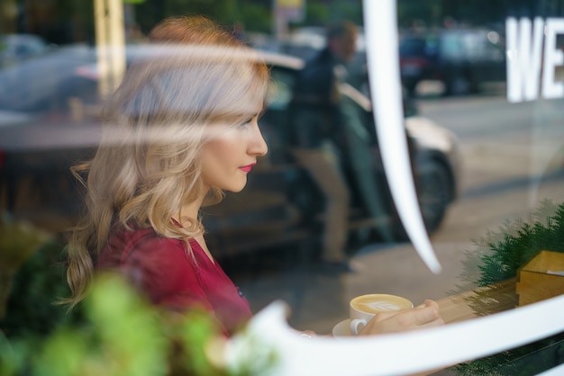 Bella donna che si siede vicino alla finestra in un caffè che beve caffè.