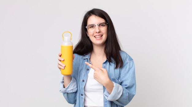 Bella donna che sorride allegramente, si sente felice e indica il lato e tiene in mano un thermos di caffè