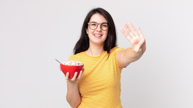 Bella donna che sorride e sembra amichevole, mostra il numero quattro e tiene in mano una ciotola per la colazione