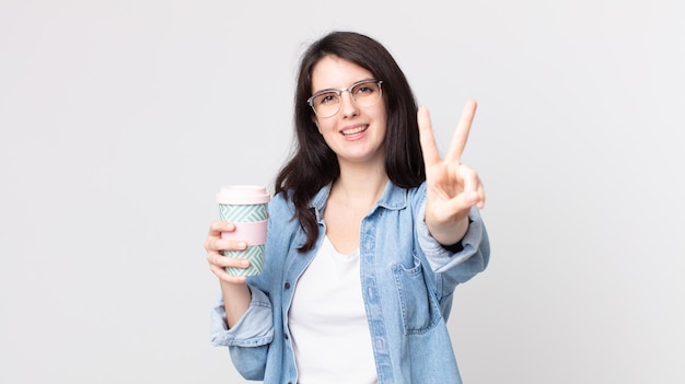 Bella donna che sorride e sembra felice, gesticola vittoria o pace e tiene in mano un caffè da asporto