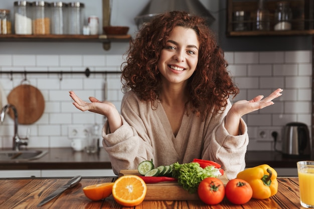 bella donna che sorride mentre cucina insalata con verdure fresche all'interno della cucina a casa