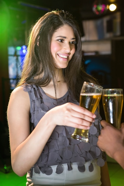 Bella donna che sorride mentre tostando il suo bicchiere di birra nella barra