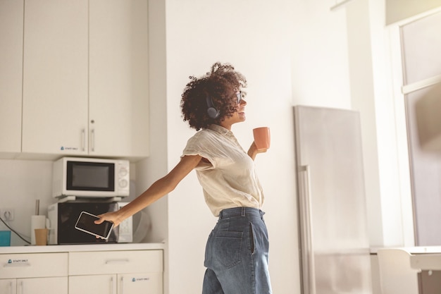 Bella donna che tiene in mano tazza e telefono mentre balla