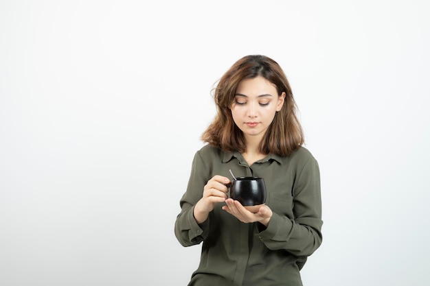 Bella donna che tiene tazza di caffè e in piedi sopra bianco. Foto di alta qualità