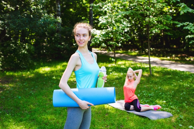 Bella donna che tiene una stuoia e una bottiglia di acqua di yoga.