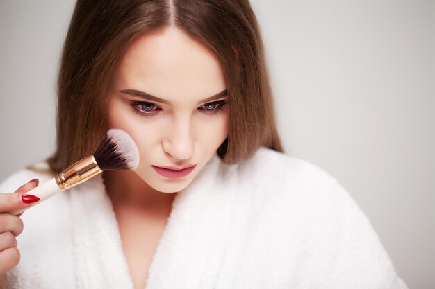 Bella donna che usa il pennello per il trucco quotidiano in bagno.