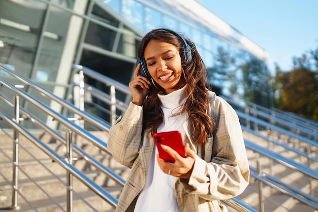 Bella donna che usa il telefono cellulare in città mentre ascolta musica attraverso le cuffie Emozioni musicali