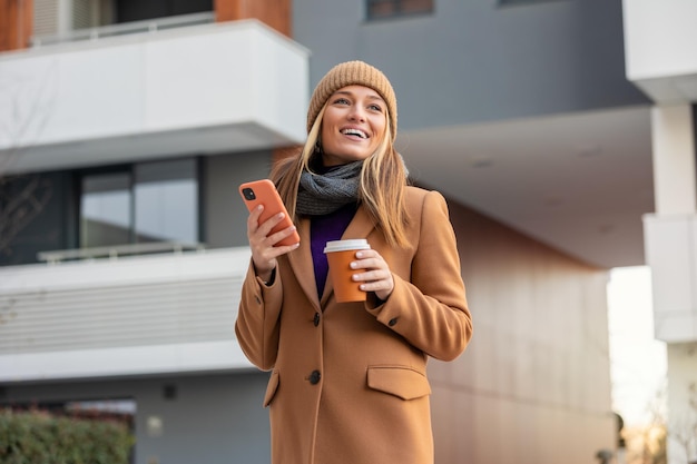 Bella donna che va a lavorare con il caffè che cammina vicino all'edificio per uffici Ritratto di donna d'affari di successo che tiene una tazza di bevanda calda