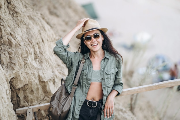 Bella donna che viaggia in cappello e occhiali da sole con rocce dietro.