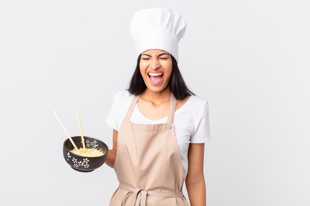 bella donna chef ispanica che grida in modo aggressivo, sembra molto arrabbiata e tiene in mano una ciotola di noodle