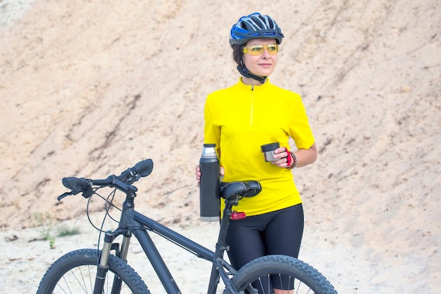 Bella donna ciclista in giallo con tè e thermos in mano