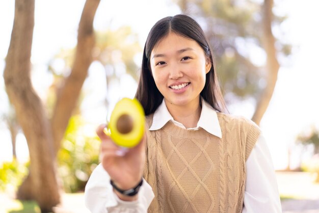 Bella donna cinese che tiene un avocado all'aperto con felice espressione