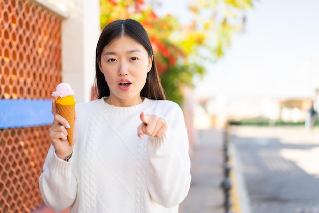 Bella donna cinese con un gelato cornetta all'aperto sorpreso e puntato davanti