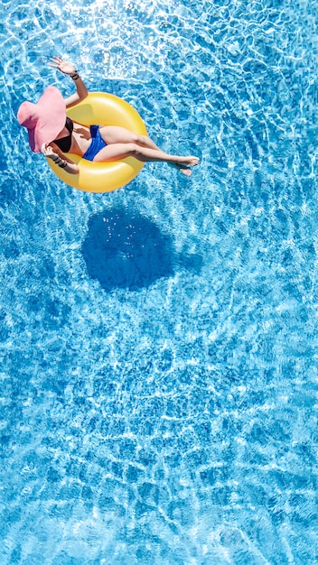 Bella donna con cappello in piscina vista aerea dall'alto, ragazza in bikini si rilassa e nuota sulla ciambella ad anello gonfiabile e si diverte in acqua in vacanza con la famiglia, località di villeggiatura tropicale