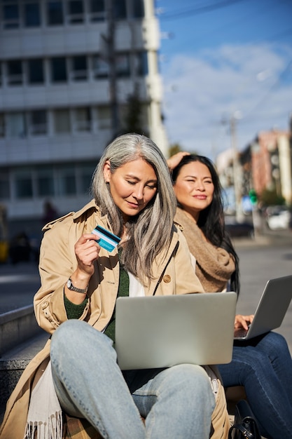 Bella donna con carta di credito utilizzando il computer portatile per strada