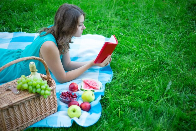 Bella donna con cestino da picnic e frutta libro di lettura nel giardino estivo