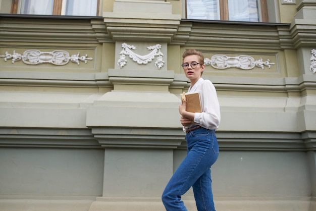 Bella donna con gli occhiali che cammina per la città con uno stile di vita da libro