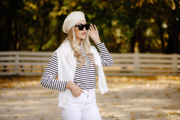 bella donna con gli occhiali e un berretto bianco nel parco in autunno