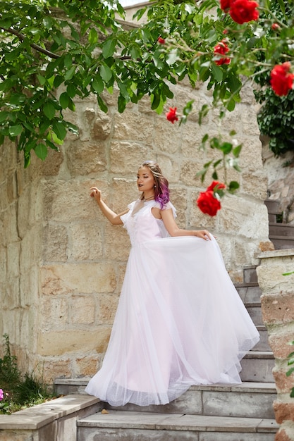 Bella donna con i capelli viola in un abito da sposa bianco cammina in giardino. Trucco naturale